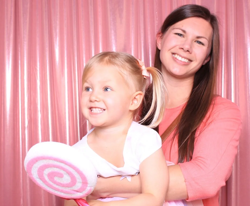 Mom and daughter with a oversized lollipop prop against a pink shimmer curtain
